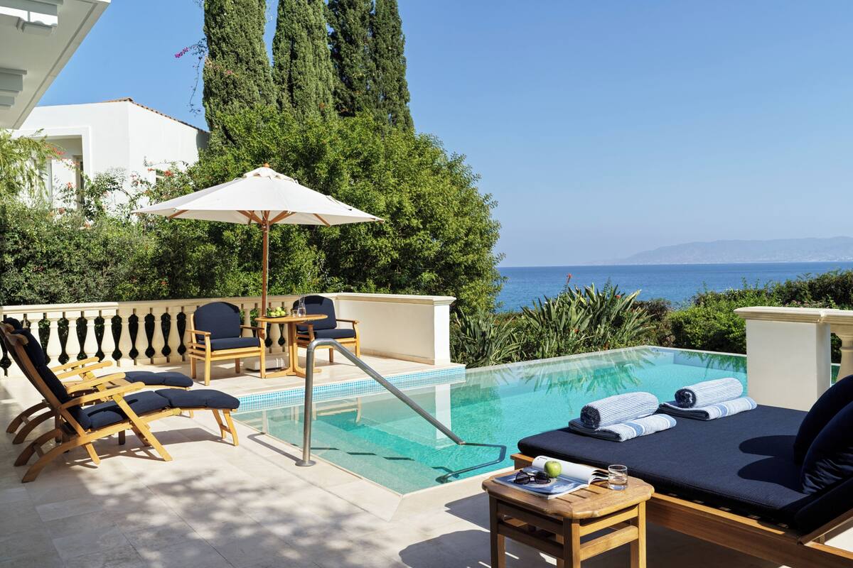 A poolside area with lounge chairs, a table with a book and glasses, and a view of the sea.