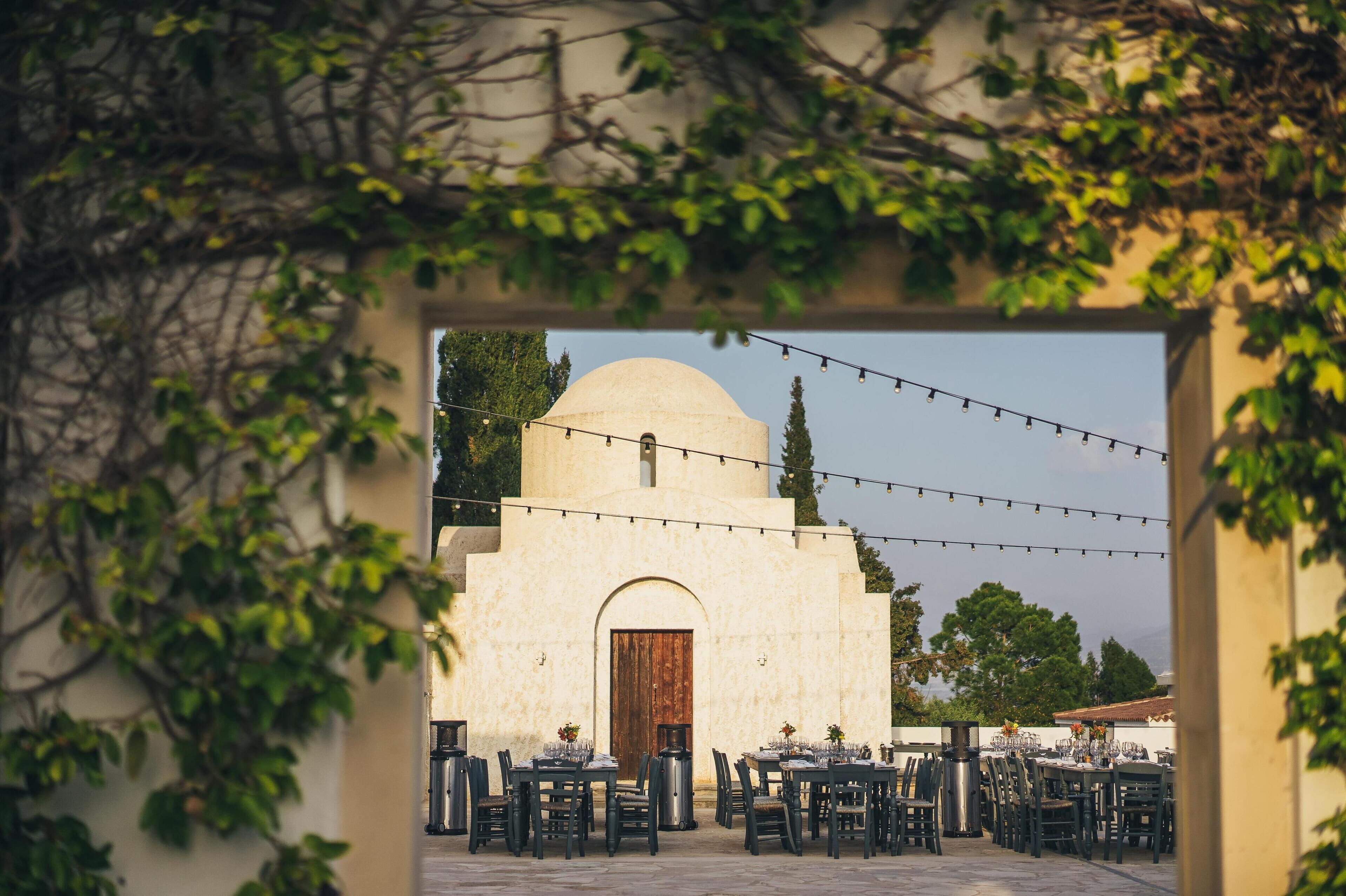 An outdoor dining area with tables and chairs arranged in front of a building with a dome and arched entrance.