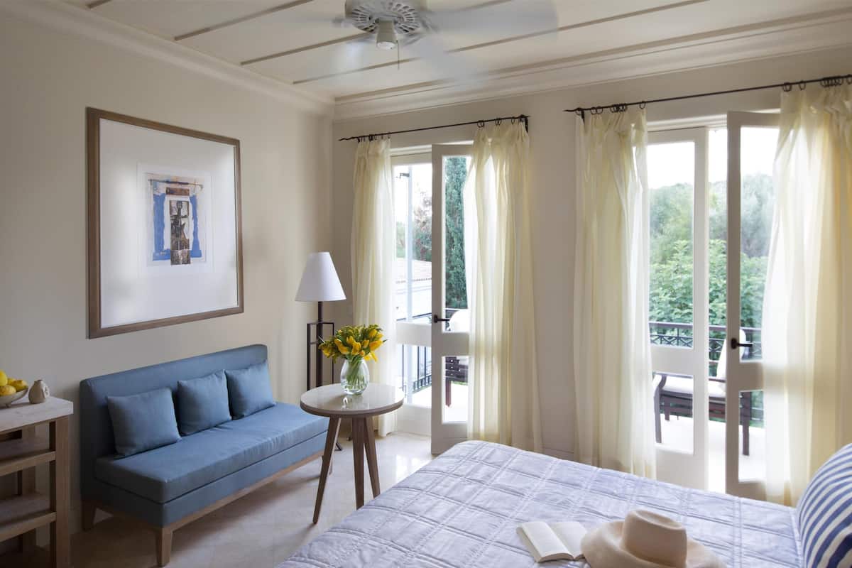 A hotel room with a bed, a blue sofa, a small table with a vase of flowers, and a framed picture on the wall.