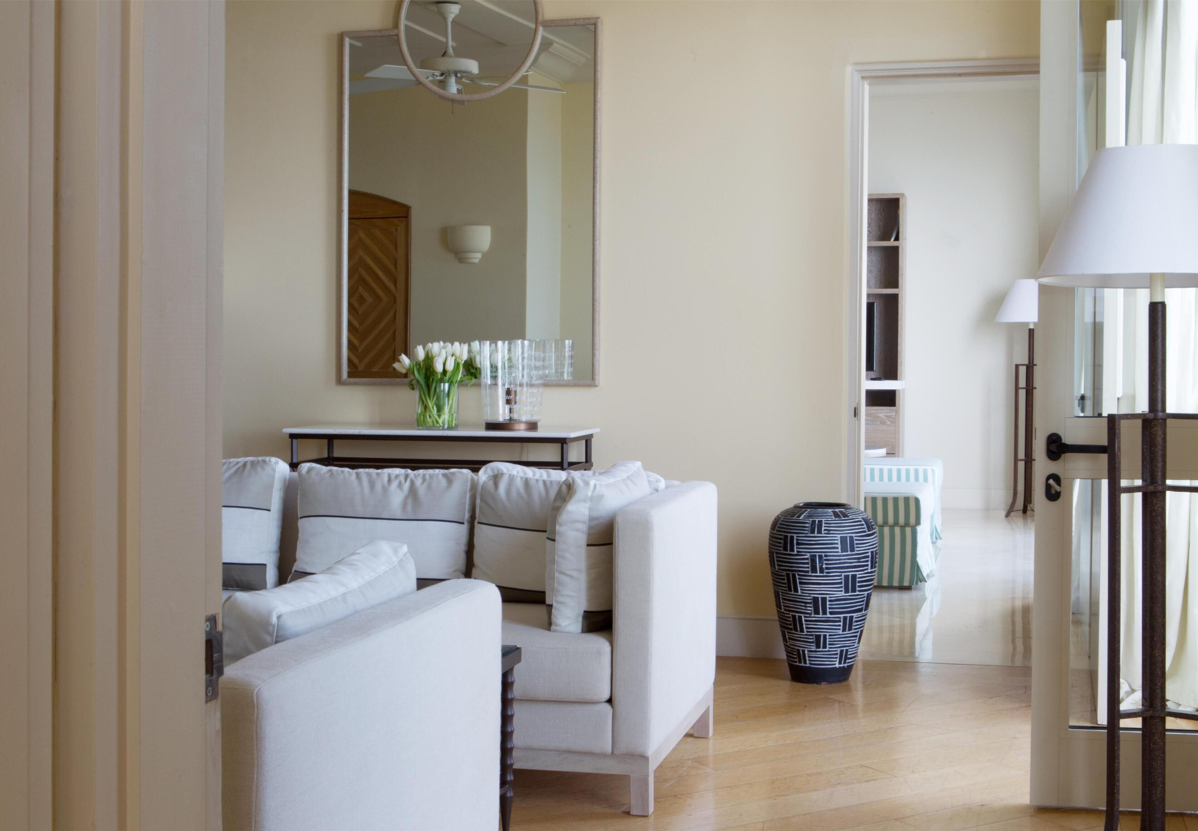 Un salon moderne avec un canapé, une table basse et un vase de fleurs. Un miroir est accroché au mur et une lampe se trouve sur une table d’appoint.