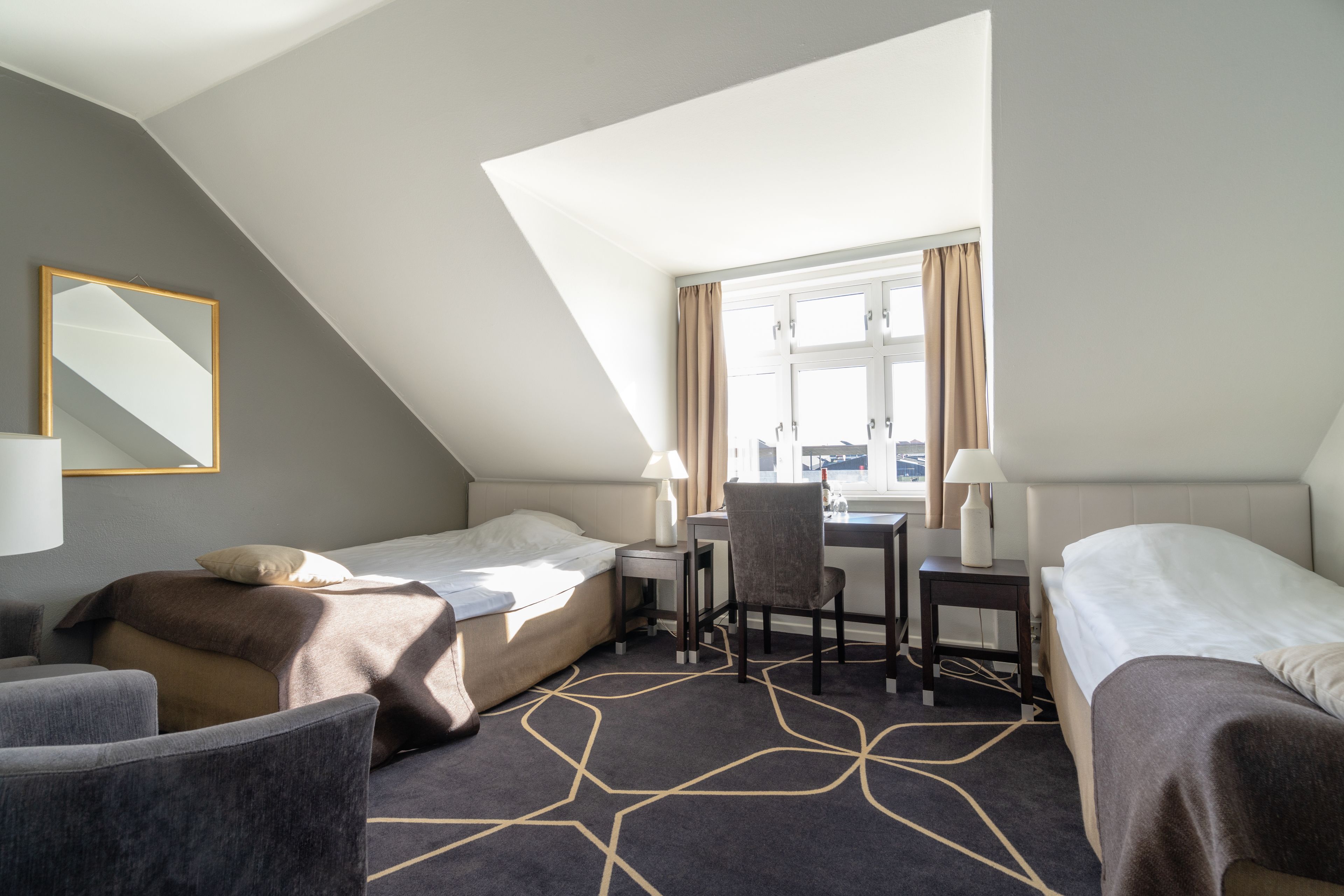 A hotel room with two beds, a desk, and a chair.