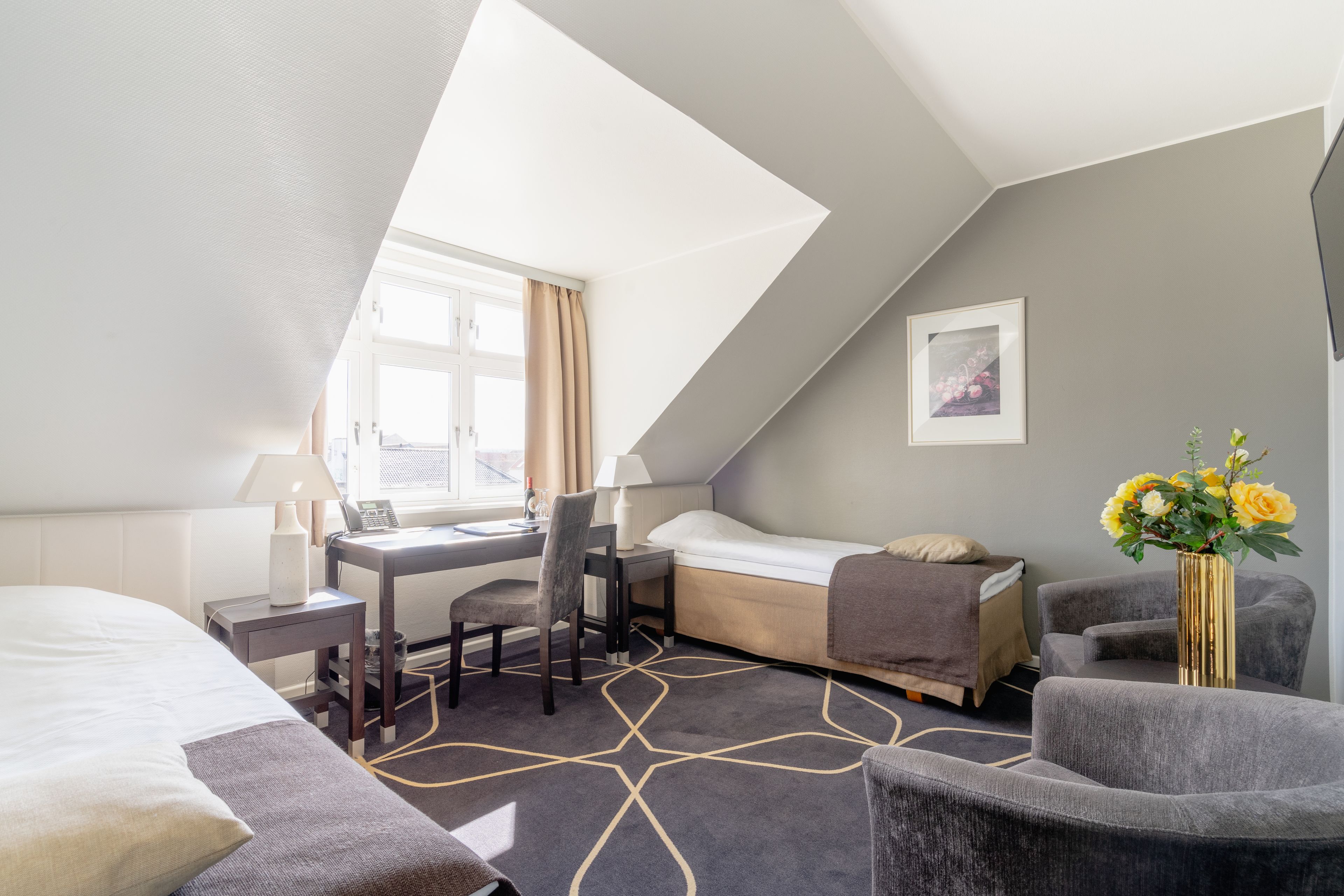 Et hotelværelse med seng, skrivebord, stol og en lille sofa.