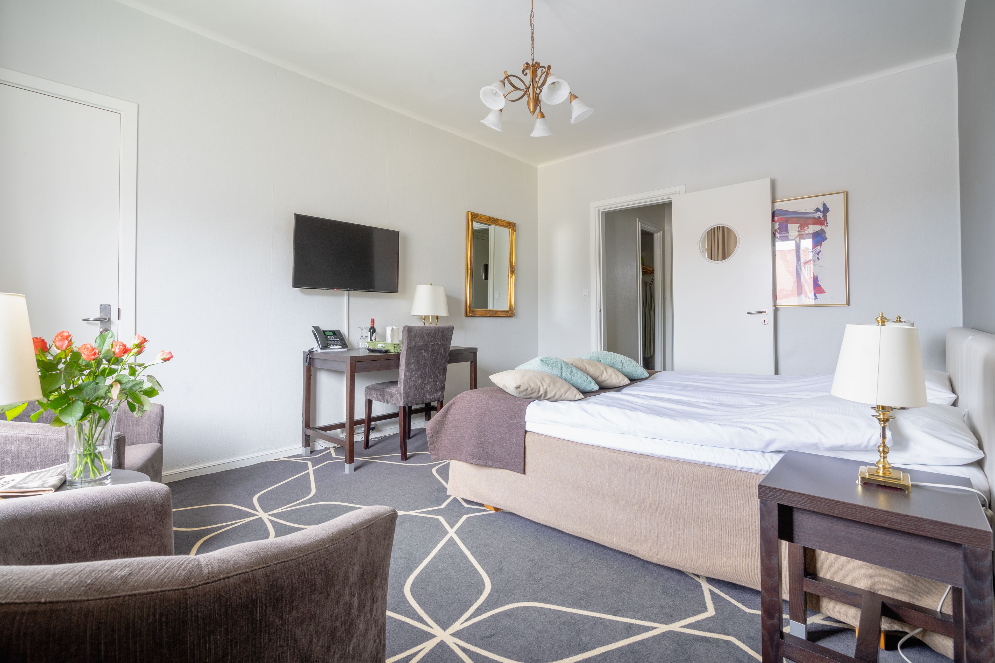 Una habitación de hotel con cama, escritorio, silla, televisión y un cuadro en la pared.
