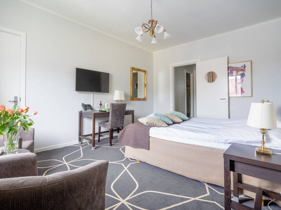 Una habitación de hotel con cama, escritorio, silla, televisión y un cuadro en la pared.