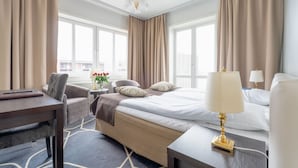 Une chambre d’hôtel comprenant un lit, des tables de chevet, un bureau, une chaise et une fenêtre avec des rideaux.
