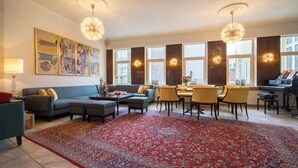 Un salon spacieux avec une grande moquette rouge, un piano et un coin repas avec des chaises jaunes.