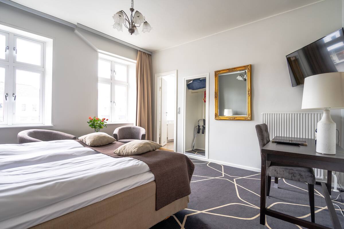 A hotel room with a large bed, a desk, a chair, a TV, and a mirror.