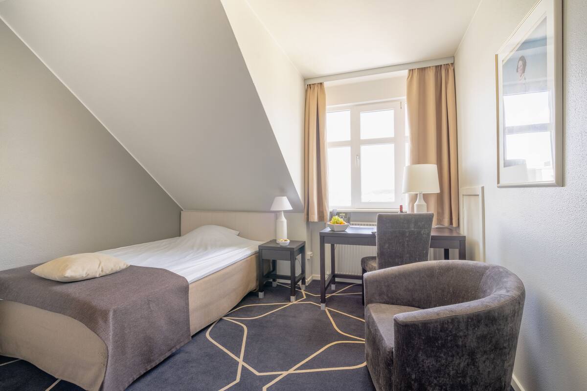 A hotel room with a bed, a desk, a chair, and a window with curtains.