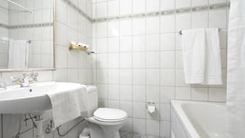Un baño con lavamanos blanco, inodoro y bañera. Se ve un perchero con una toalla colgada.