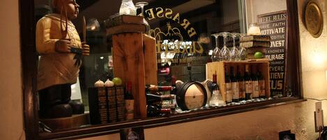 Un bar con un bancone in legno, bottiglie di vino, bicchieri e una statua decorativa.
