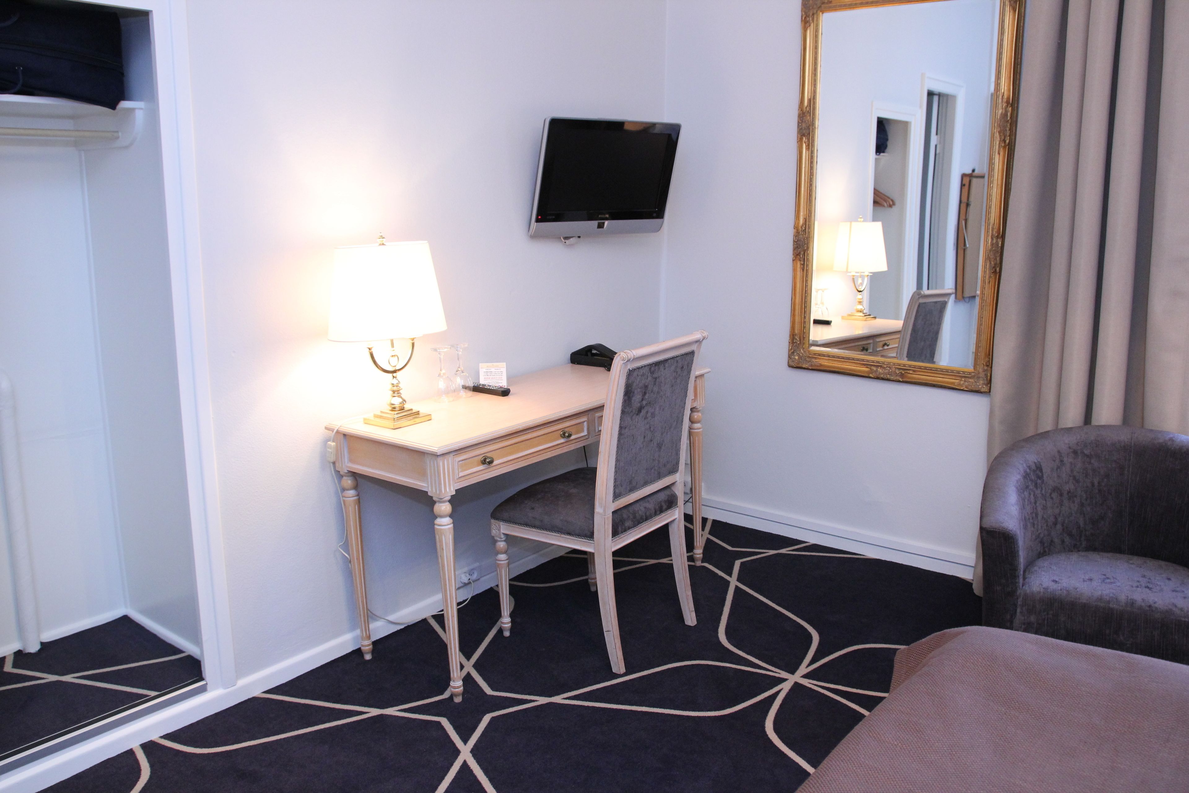 Ein Hotelzimmer mit Schreibtisch, Stuhl, Fernseher und einem großen Spiegel.