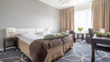 A hotel room with a large bed, a desk, a chair, a small table, and a window with curtains.