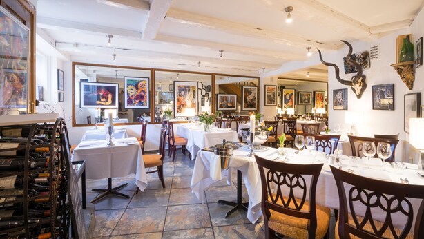 Un restaurant doté de nombreuses tables et chaises, de présentoirs à vin et d’œuvres d’art accrochées aux murs.