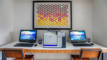 A workspace with two laptops, a printer, and a framed abstract art piece on the wall.