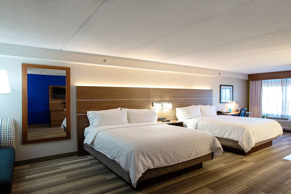 A hotel room with two beds, a large mirror, a TV, and a desk with a lamp.