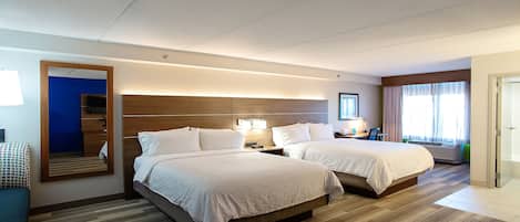Habitación de hotel con dos camas, un espejo grande, un televisor y un escritorio con lámpara.