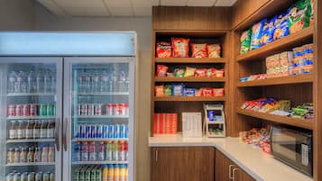 A self-service snack and drink station with refrigerated beverages, snack packs, and a microwave.