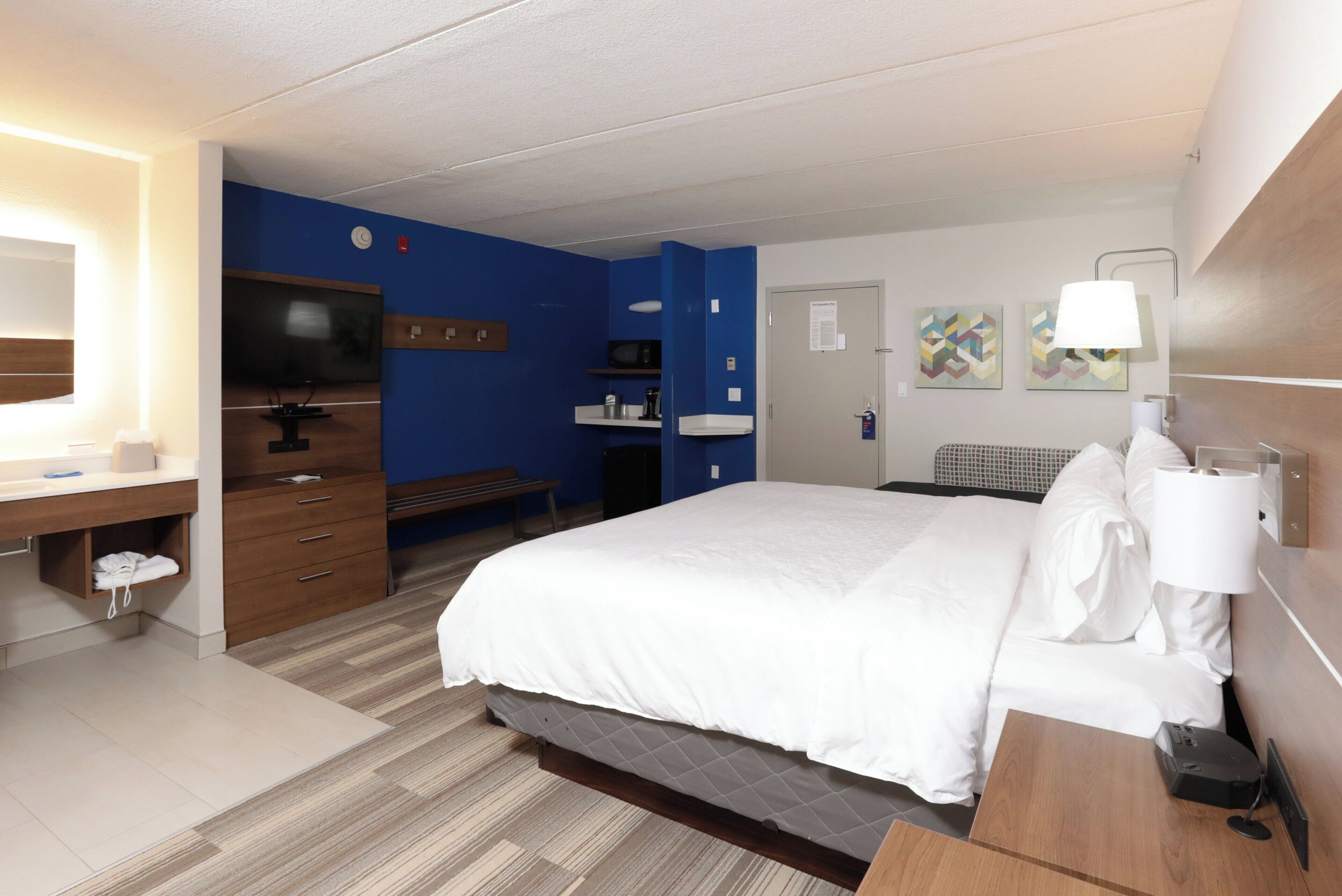 A hotel room with a bed, desk, chair, TV, and a bathroom.