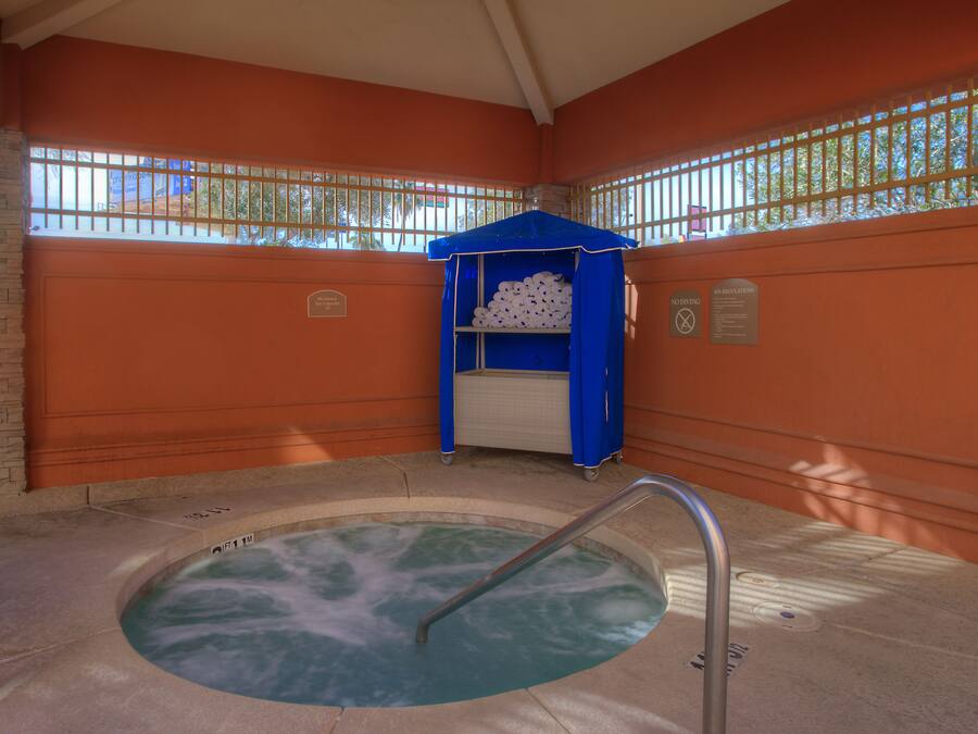Zona de hidromasaje con toldo azul, una escalera metálica y una ventana con barrotes.