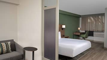Een hotelkamer met een bed, een klein rond tafeltje, een bank, een nachtkastje, een lamp en een groene stoel.