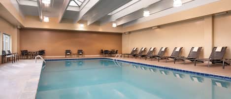 A swimming pool with lounge chairs and a skylight ceiling.