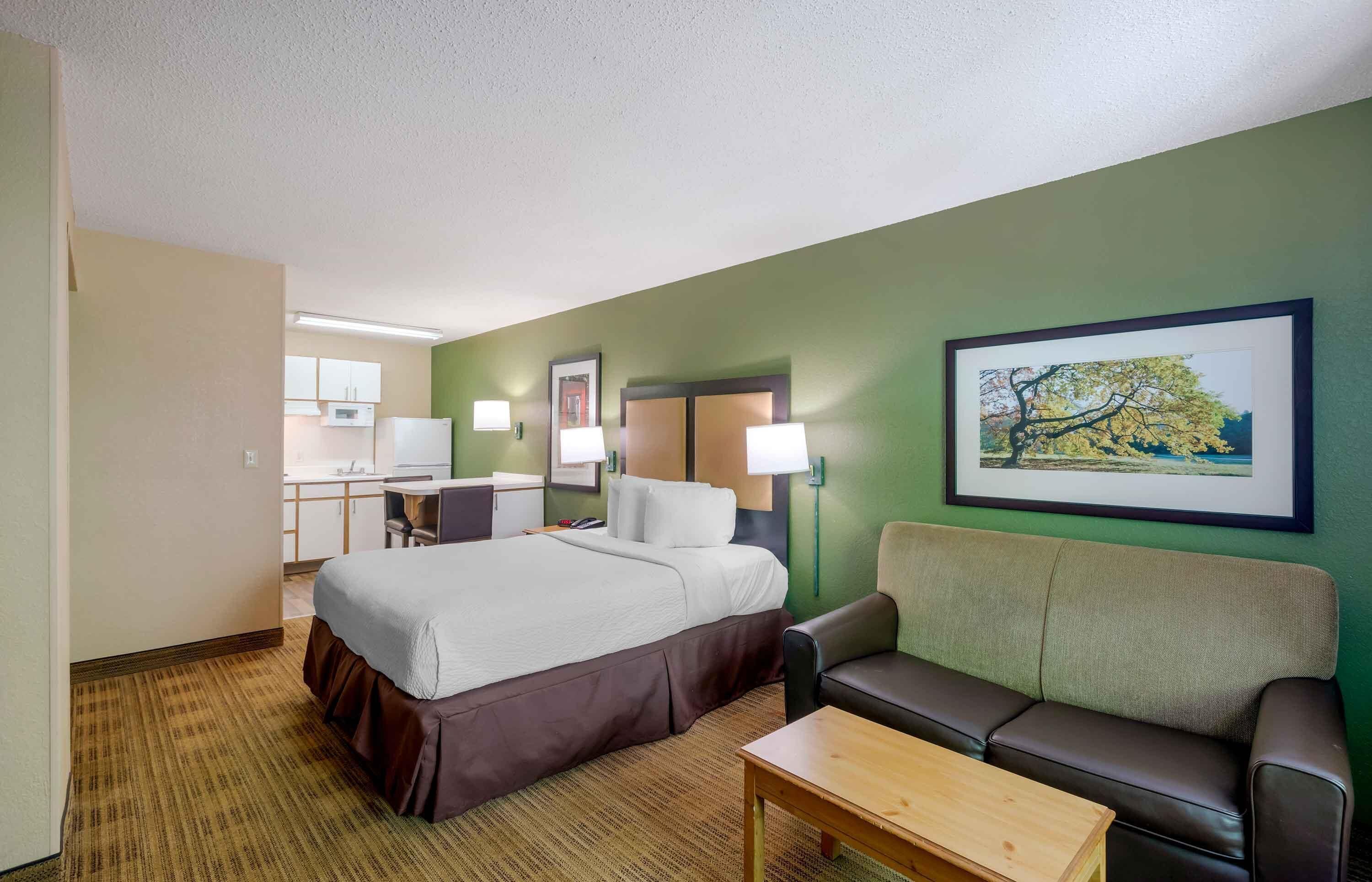 Une chambre d’hôtel avec un lit, un bureau, une chaise, un canapé et un tableau au mur.