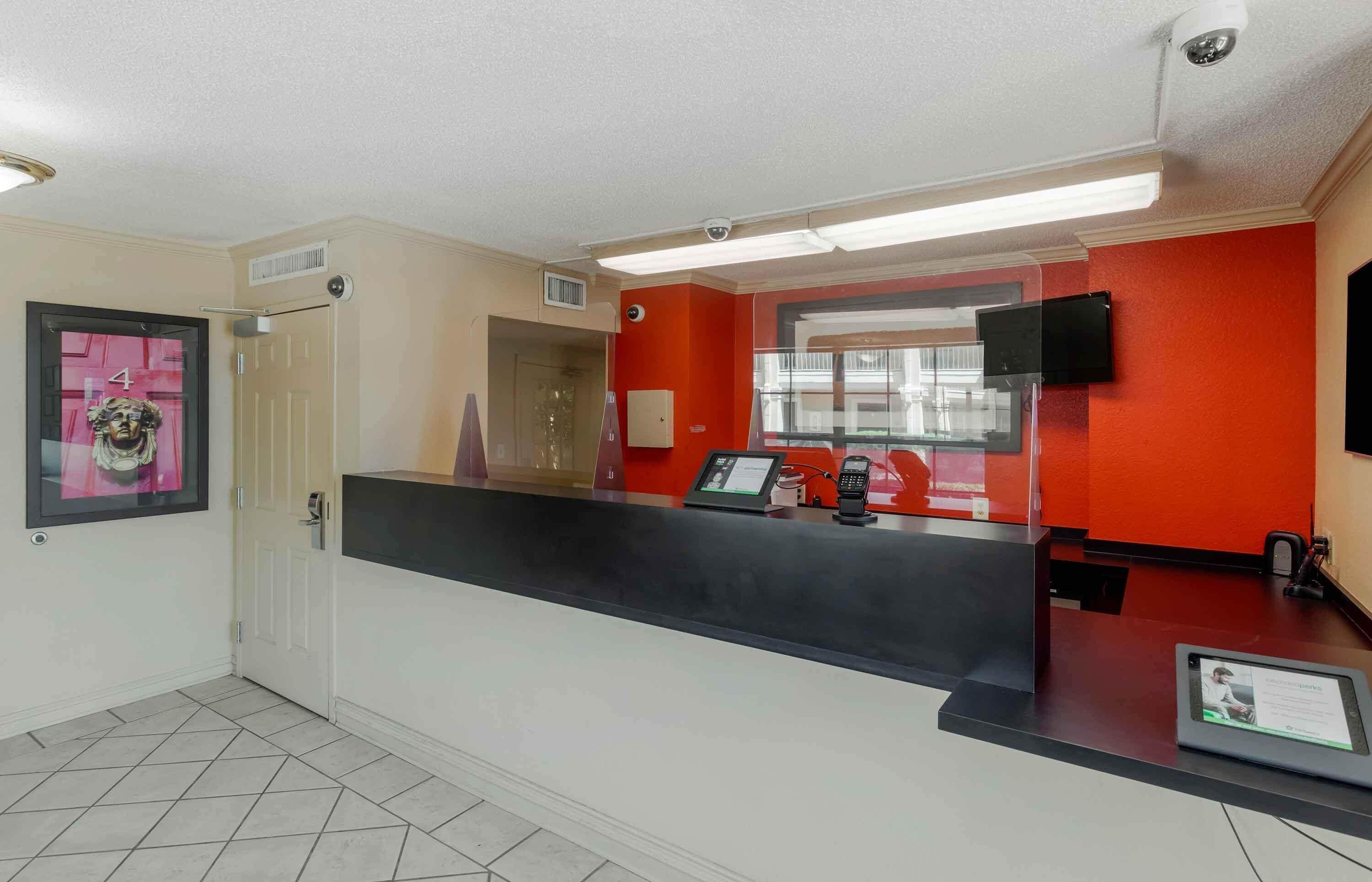 A reception area with a black counter, a red wall, a door, and a window with a view.