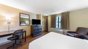 A hotel room with a large bed, a desk with a chair, a television, a dresser, and a window with curtains.