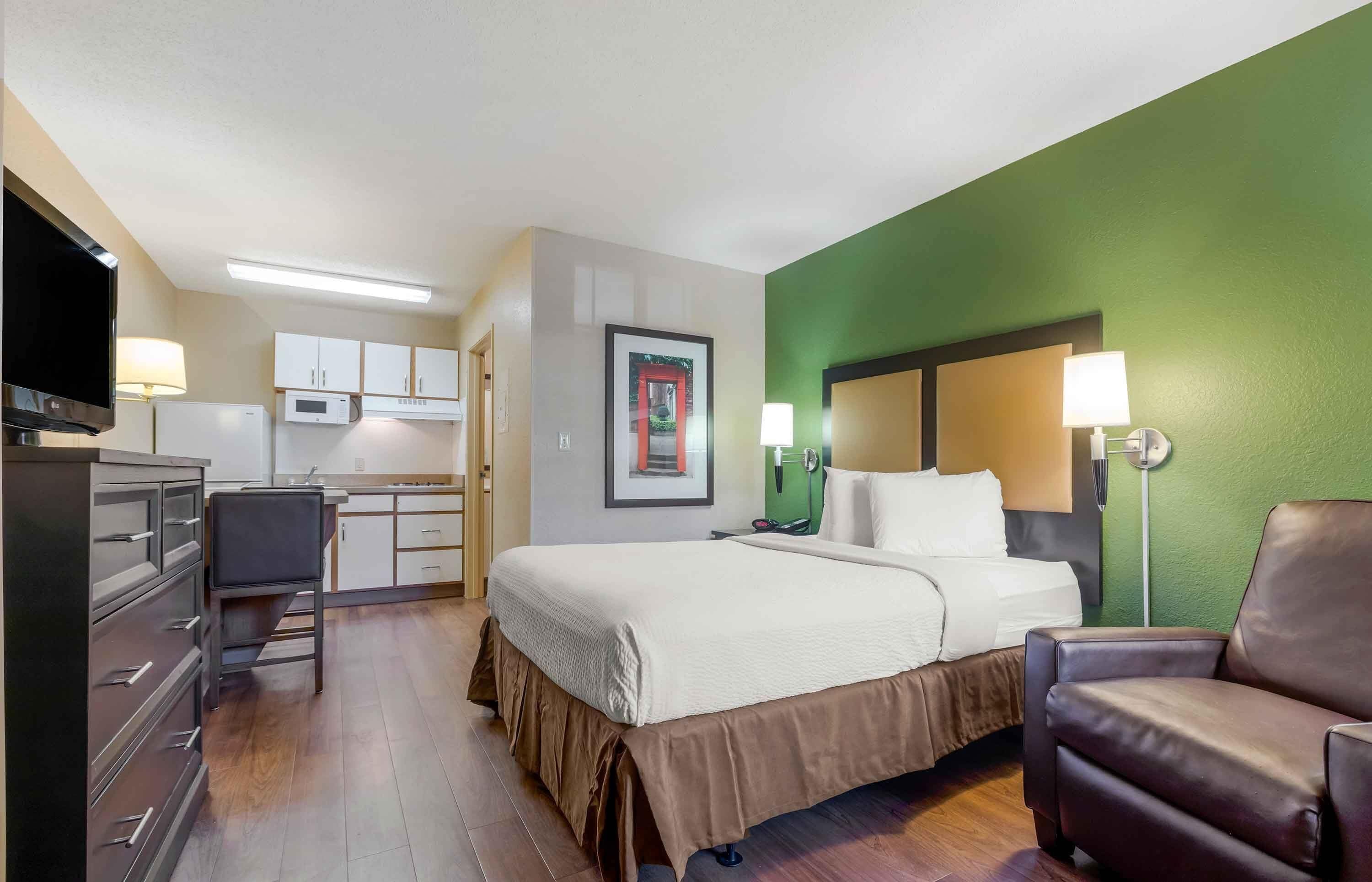 A hotel room with a bed, a desk, a television, and a kitchenette.