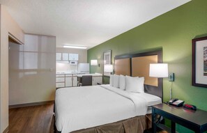 A hotel room with a bed, a desk, a chair, a telephone, and a wall-mounted lamp. - Extended Stay America Select Suites Atlanta Perimeter Hammon (Atlanta)