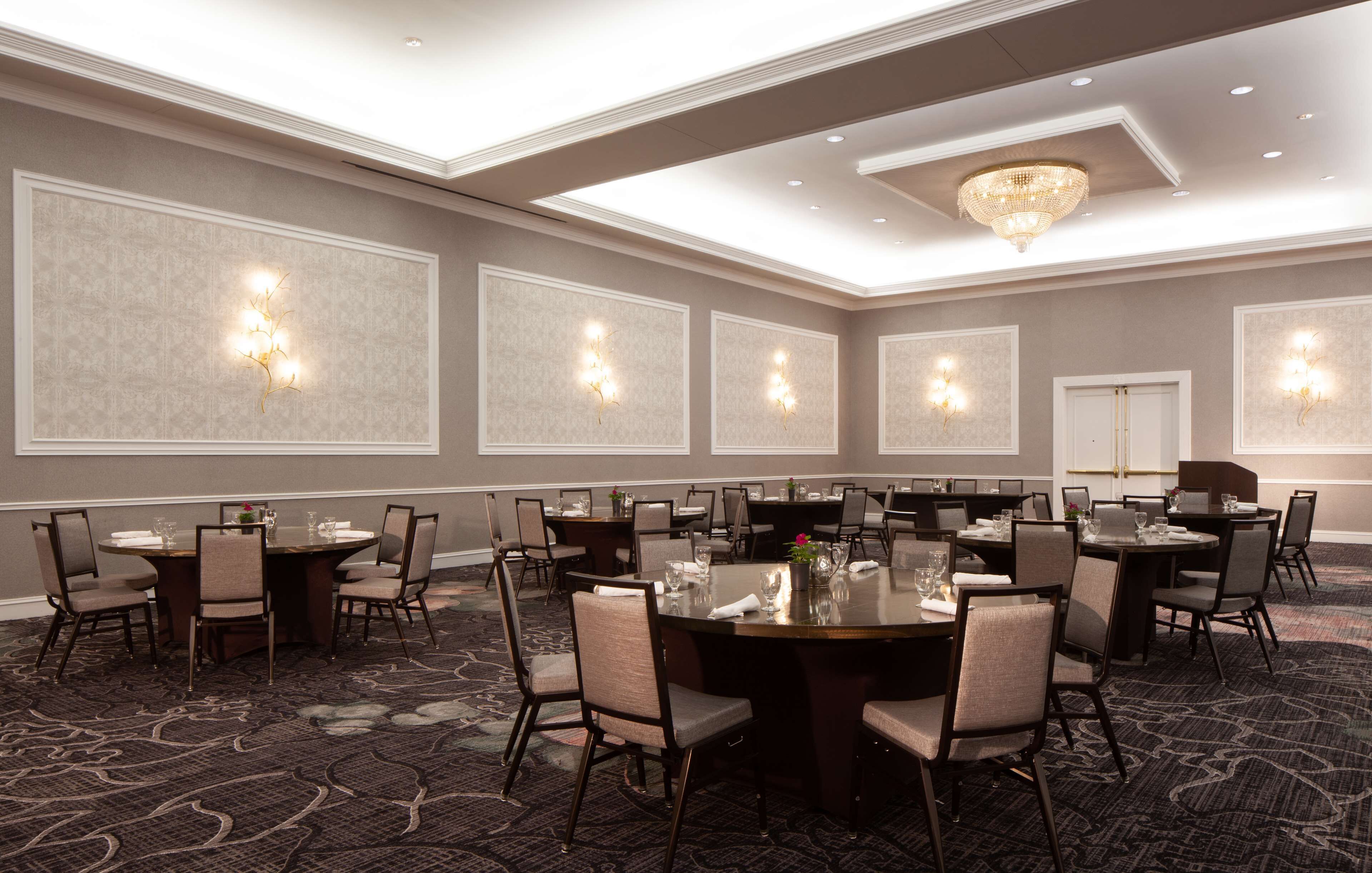 A conference room with multiple tables and chairs, recessed lighting, and a chandelier.