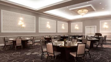 Un salón de conferencias con varias mesas y sillas, iluminación empotrada y un candelabro.