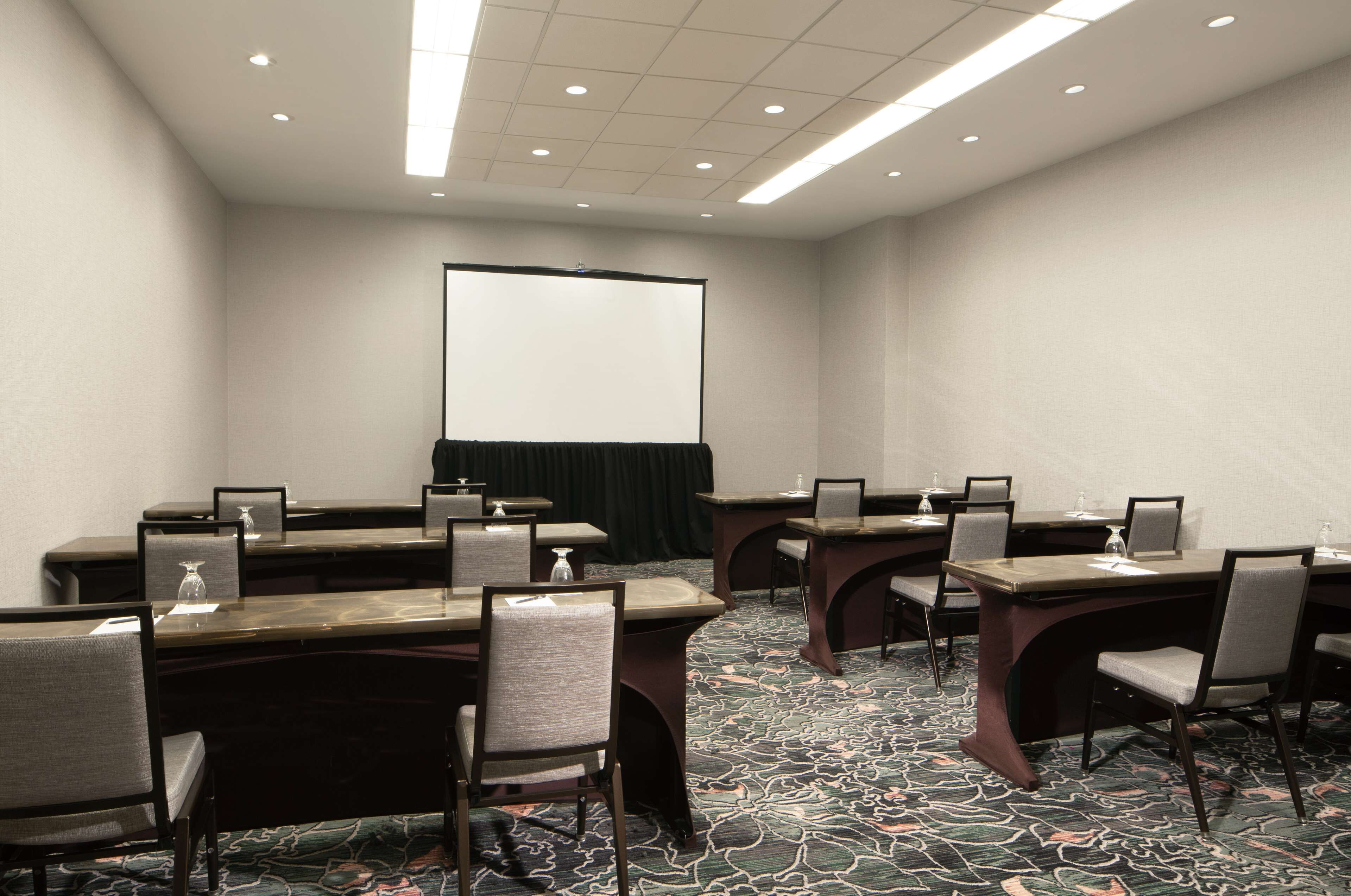 A conference room with a large table, chairs, a projector screen, and a carpeted floor.