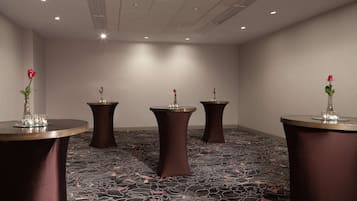 A conference room with four round tables, each with a vase of a red rose and a glass. The room has a patterned carpet and recessed ceiling lighting.