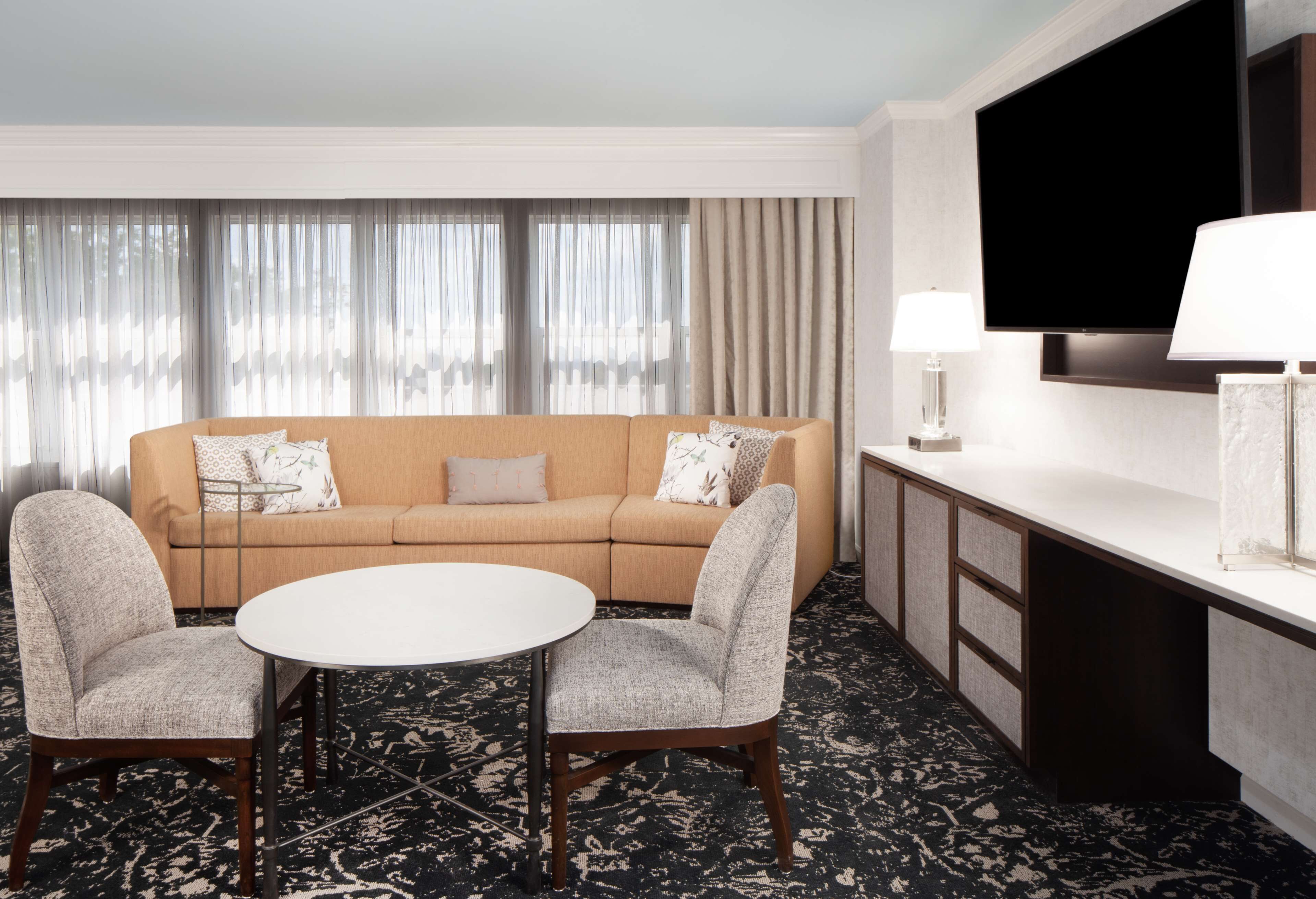 A hotel room with a beige sofa, two armchairs, a round table, a TV, and a minibar.