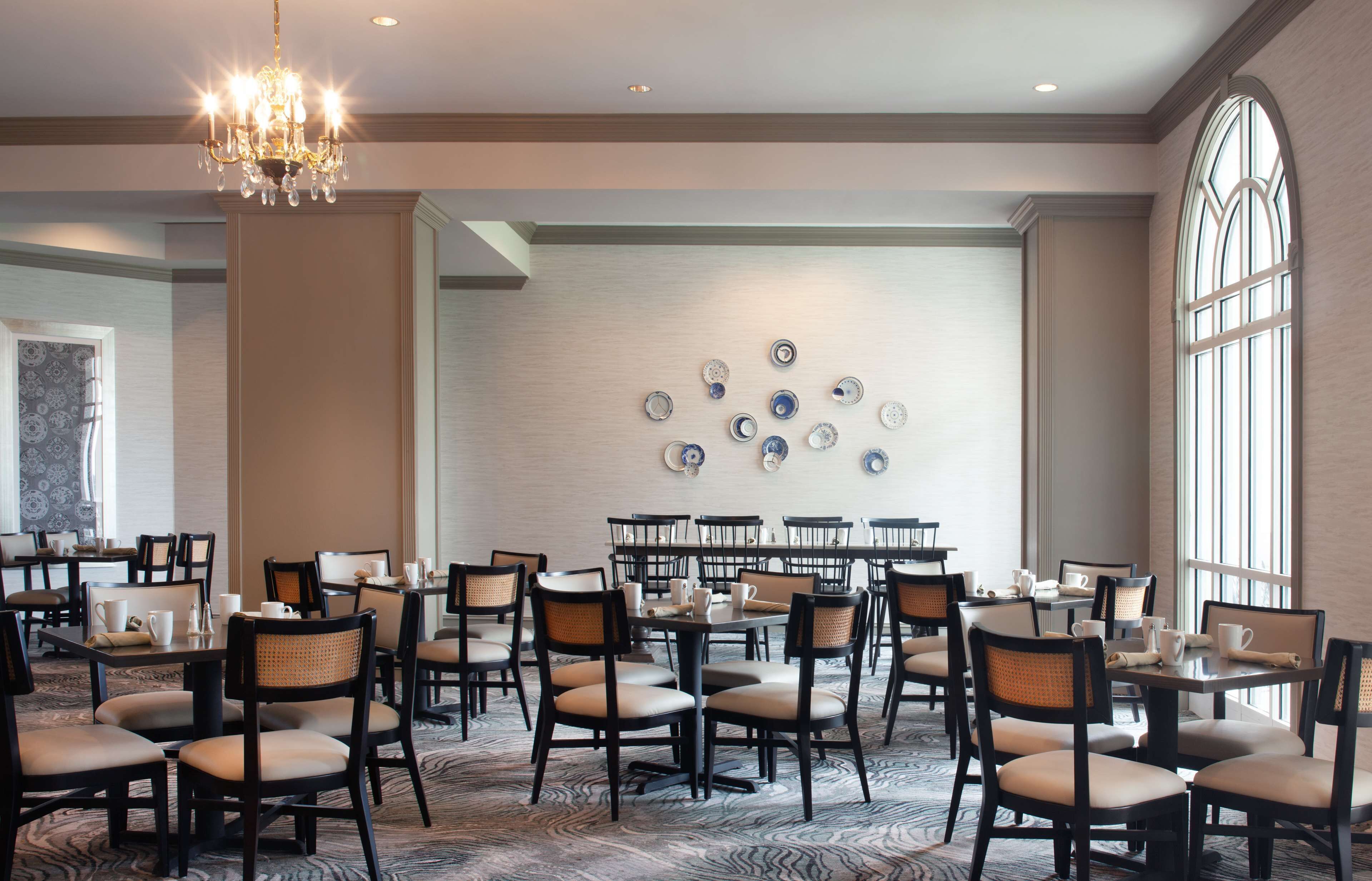 Une salle à manger d’hôtel avec plusieurs tables et chaises, un lustre et un mur décoré d’assiettes.