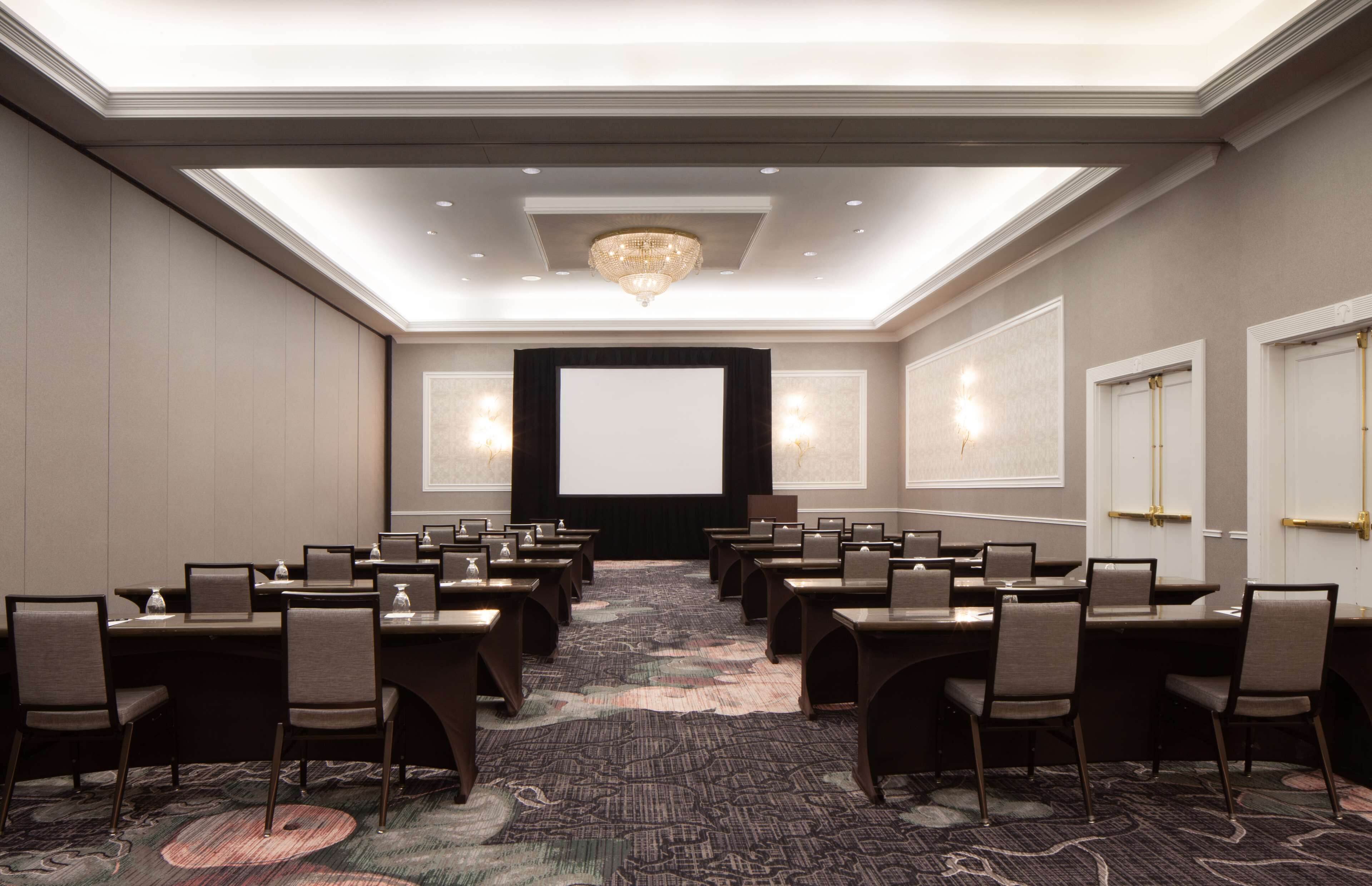 A conference room with a large screen, multiple tables, and chairs arranged for a meeting.