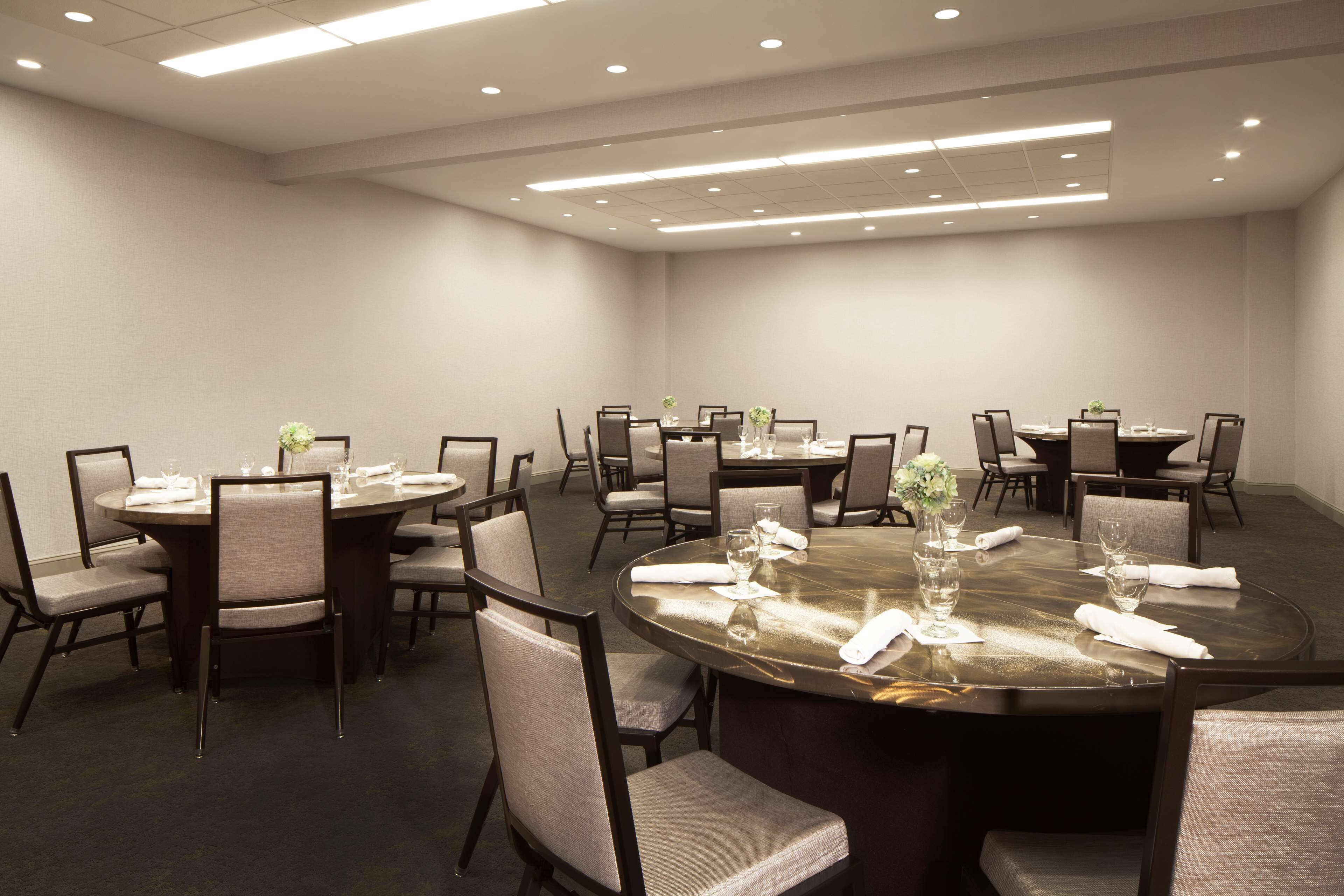 A conference room with multiple round tables, each set with chairs, glasses, and a vase of flowers.