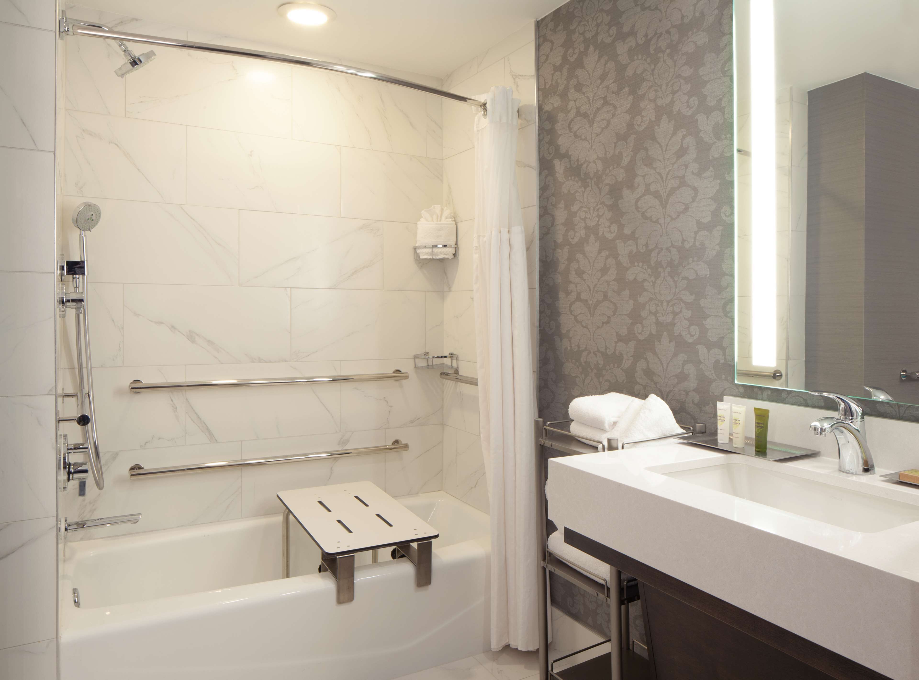 A modern bathroom with a walk-in shower, grab bars, a bathtub, and a vanity with a mirror.
