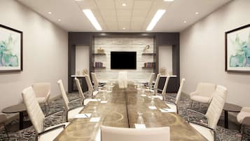 Une salle de conférence avec une longue table, des chaises blanches, un téléviseur à écran plat et des étagères à livres.
