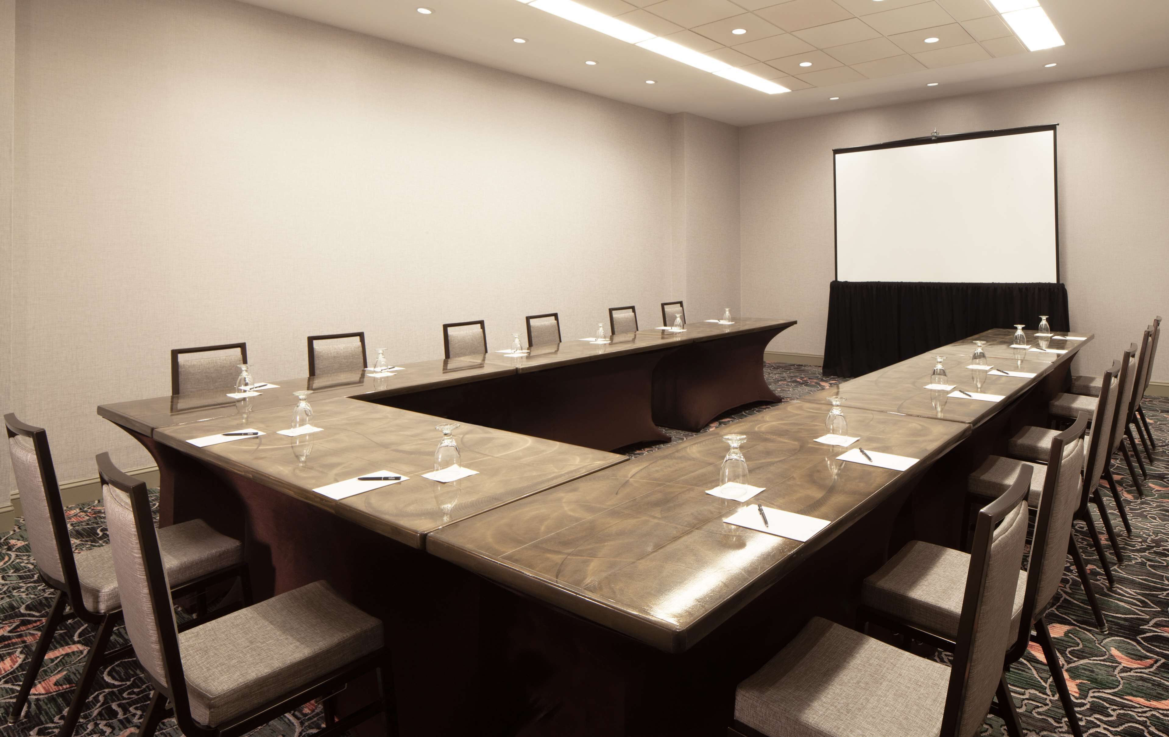 A conference room with a long table, chairs, a projector screen, and a carpeted floor.