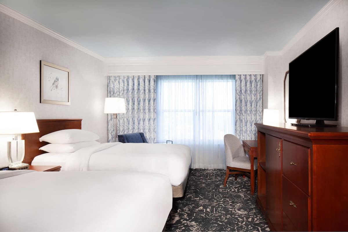 A hotel room with two beds, a television, a desk, and a chair.