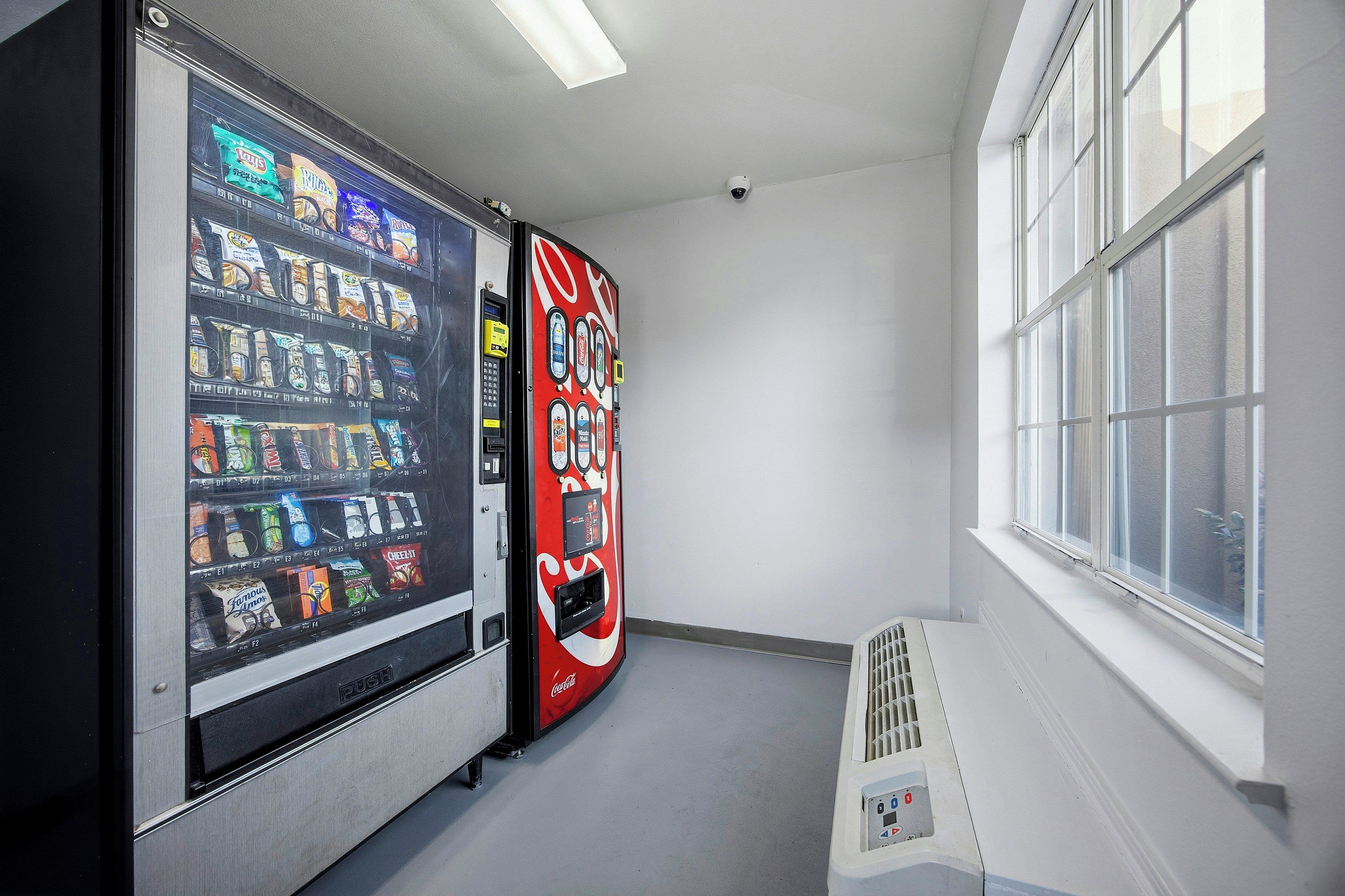A vending machine with a Coca-Cola logo, a window with blinds, and a vent on the floor.