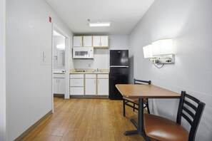 A compact kitchen with white cabinets, a microwave, and a black refrigerator. - HomeTowne Studios by Red Roof Atlanta – Peachtree Corners (Peachtree Corners)