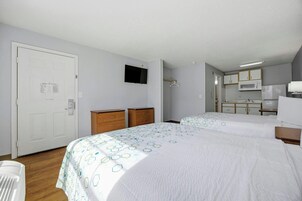 A hotel room with two beds, a wardrobe, a television, and a kitchenette.