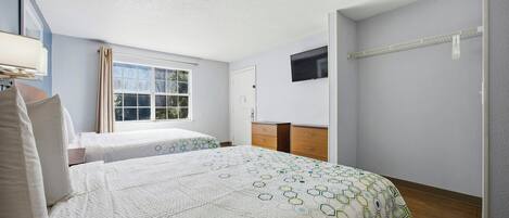 Una habitación de hotel con dos camas, una ventana con cortinas, un televisor montado en la pared y un aparador de madera.