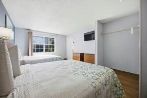 Una habitación de hotel con dos camas, una ventana con cortinas, un televisor montado en la pared y un aparador de madera.