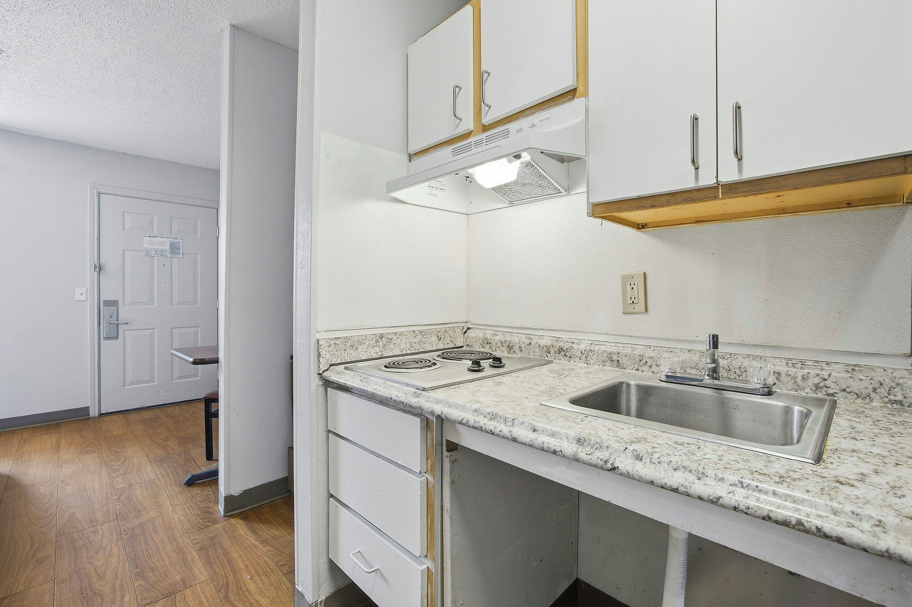 A kitchen with white cabinets, a stainless steel sink, a stove, and a wooden countertop.