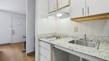 A kitchen with white cabinets, a stainless steel sink, a stove, and a wooden countertop.
