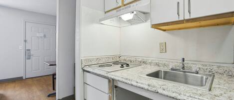 A kitchen with white cabinets, a stainless steel sink, a stove, and a wooden countertop.